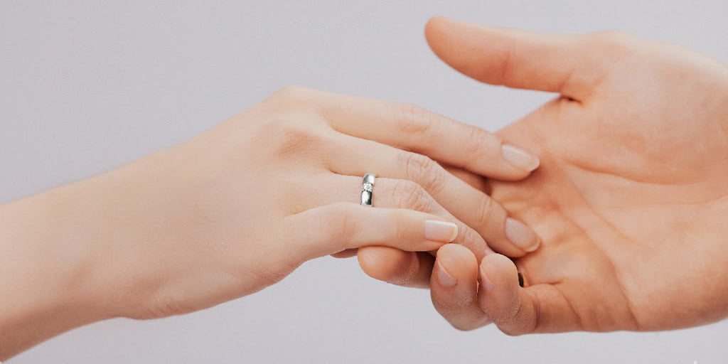 Paar hält Hände - Weißgoldener Ring mit Diamant am Finger 